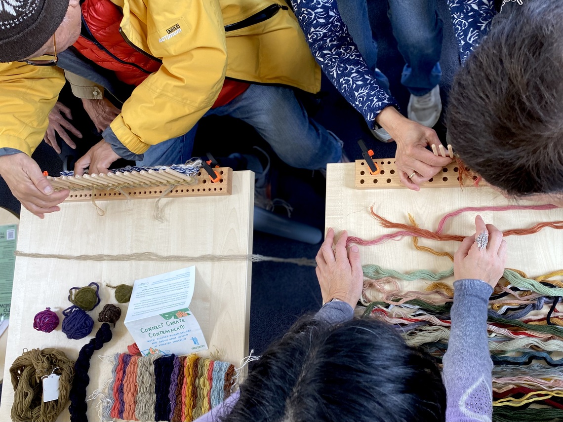 A group of elderly people weaving on peg looms