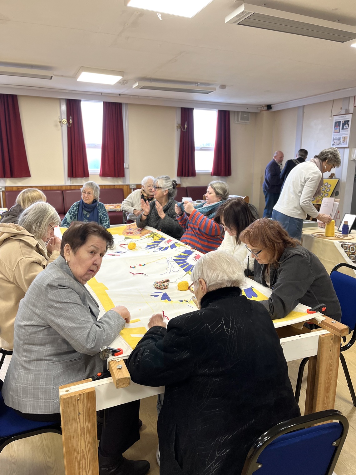 A group of women stitching a tapestry in a hall