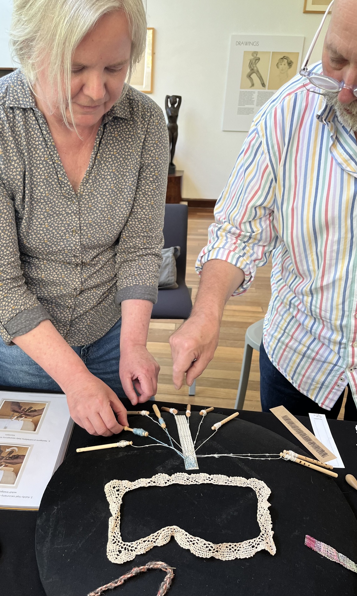 Two people demonstrating the basic technique of bobbin lace